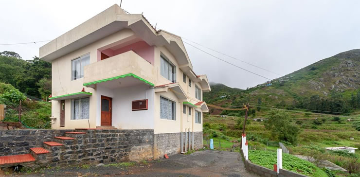 Exterior view of a cottage surrounded by mountains in Ooty