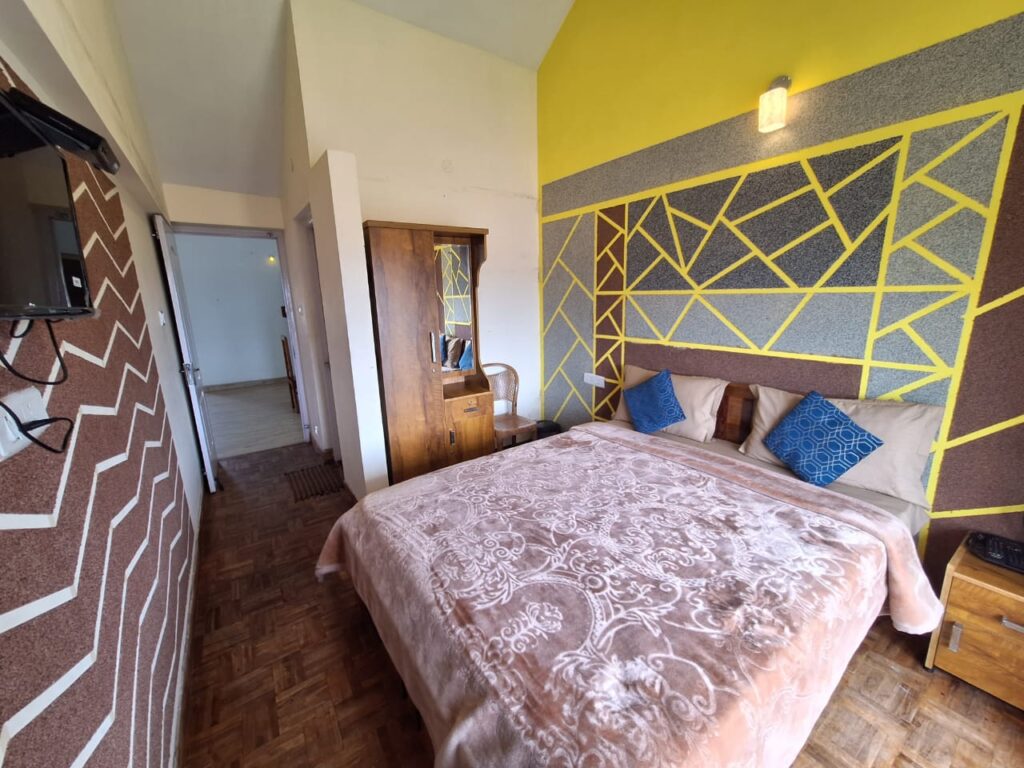 Cozy Ooty cottage bedroom featuring a double bed, geometric accent wall design, wooden furniture, and warm natural lighting