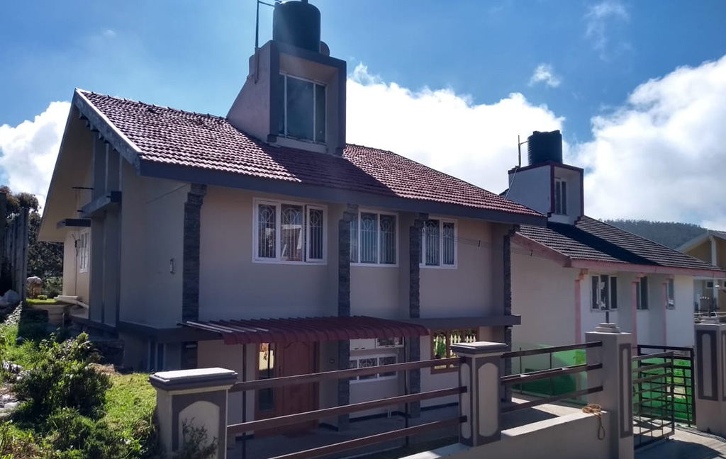 Hill cottage with red tiled roof, balcony, and scenic mountain view under blue sky.