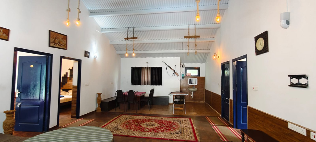 Interior view of a heritage-style Ooty cottage with wooden flooring, hanging lights, traditional decor, and bedroom entrances