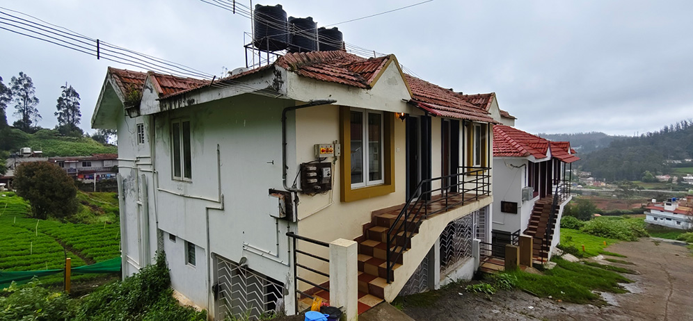 Independent hillside cottage in Ooty with red tiled roof and green plantation surroundings