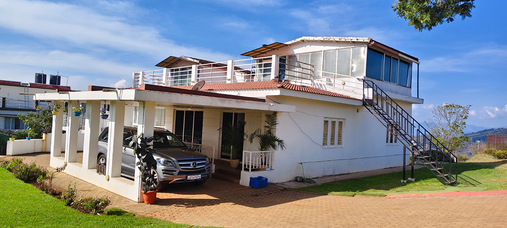 White cottage with terrace, external staircase, garden lawn, and car parked under a covered porch.