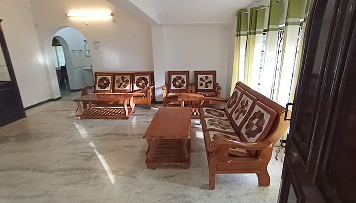Spacious family cottage living room with wooden sofa set, marble flooring, coffee table, and large windows with green curtains