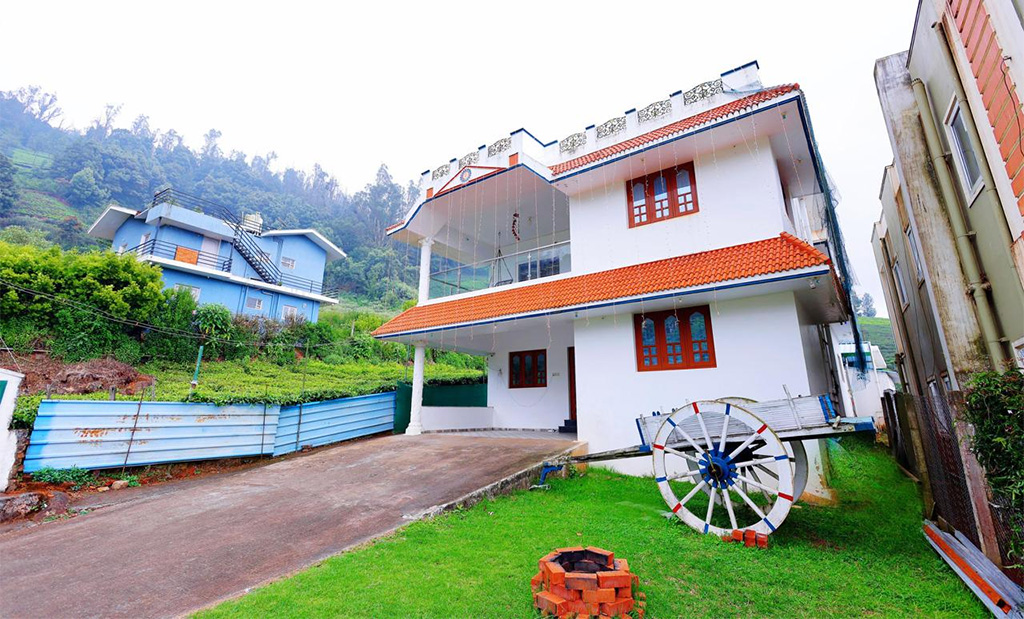 White private cottage in Ooty with red tiled roof, glass balcony, lawn and hill view
