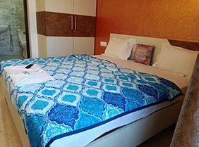 Bedroom with king size bed, blue patterned blanket, pillows, wardrobe, and attached bathroom