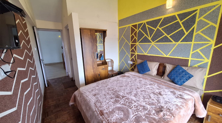 Small bedroom with a single bed, wooden wardrobe, patterned accent walls, and blue decorative pillows