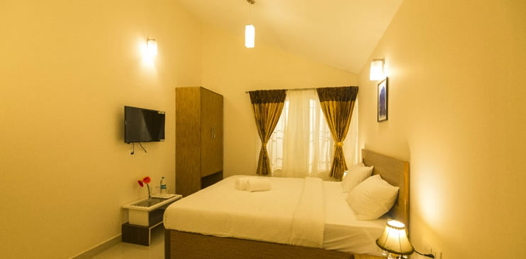 Cozy cottage bedroom with neatly made bed, wall-mounted TV, wardrobe, and soft ambient lighting for a relaxing stay