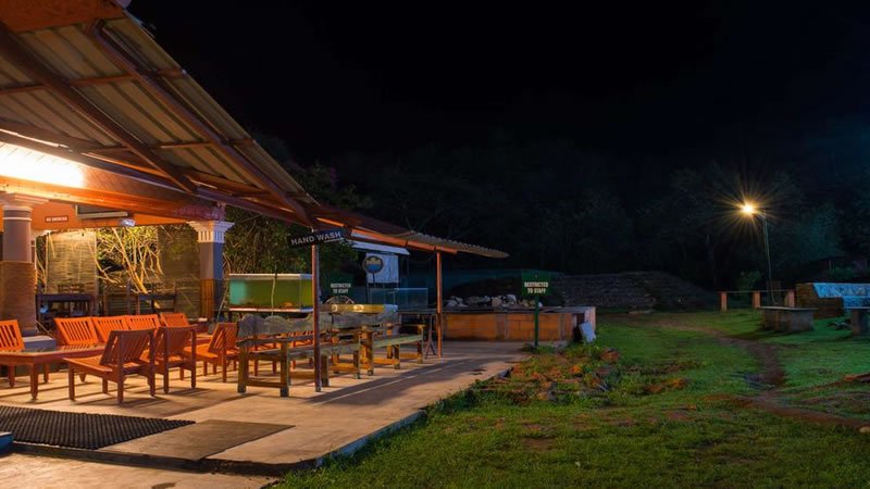Outdoor dining and seating area illuminated at night beside a green lawn