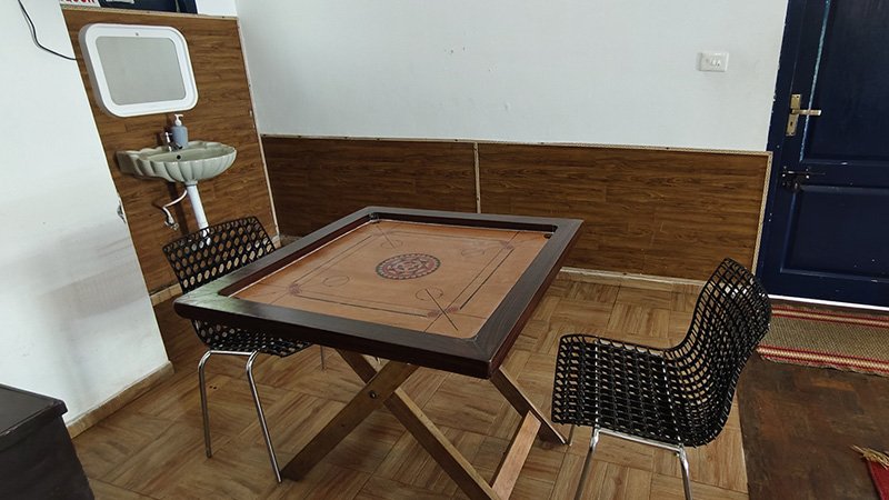 Indoor recreation area with carrom board table and seating chairs for guests