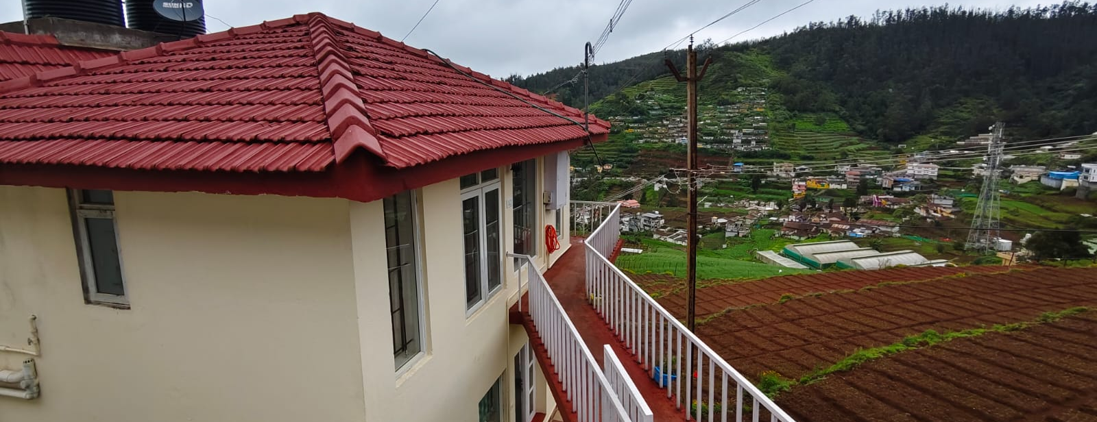 Ooty cottage with red tiled roof overlooking green hills and farmland