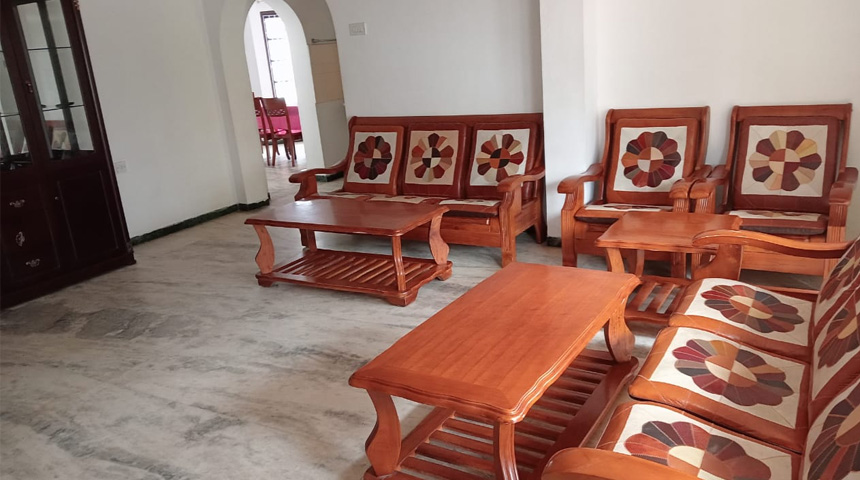 Spacious homestay living room with wooden sofa set and coffee tables in Ooty
