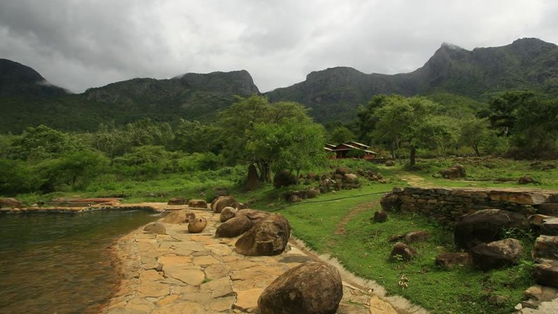 Natural pool surrounded by rocks, green trees and dramatic mountain landscape