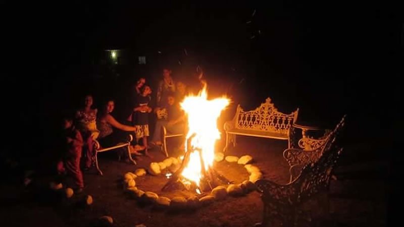 Outdoor campfire area with guests seated around a large bonfire at night