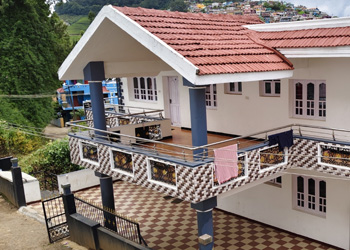 Exterior view of Sasi Cottage featuring a duplex house with red tiled roof, spacious balcony, and hill-view surroundings