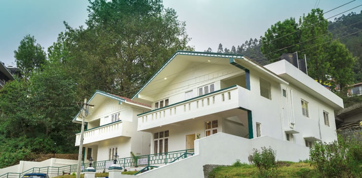 White hill-view cottage surrounded by trees, featuring balconies and sloped roofs in a peaceful mountain setting