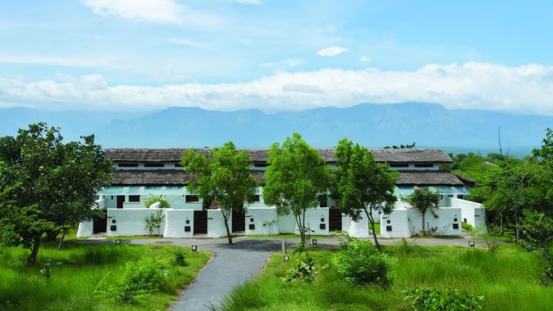 White cottages surrounded by green trees and grass with mountains in the distance