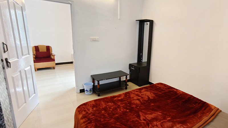 Bedroom with red blanket bed, dressing mirror, table and door to hall