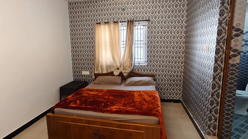 Bedroom with wooden double bed, red blanket, pillows, window and curtains
