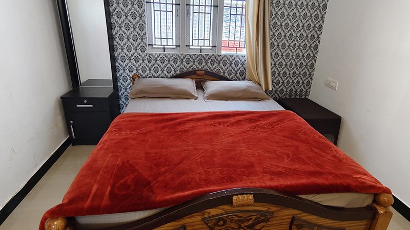 Double bed bedroom with red blanket, pillows, dressing mirror and window