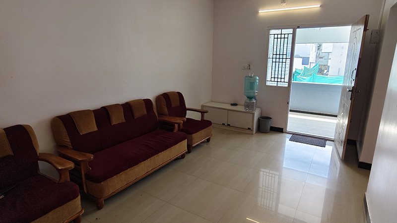 Spacious living hall with sofa set, tiled floor, water dispenser and balcony door